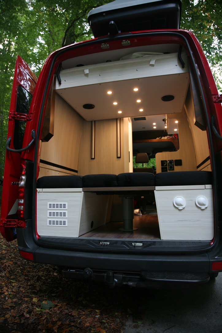 Sprinter Camperausbau – Blick durch die Hecktür auf umgeklappte Liegefläche, Hubtisch und Hubbett im Heckbereich